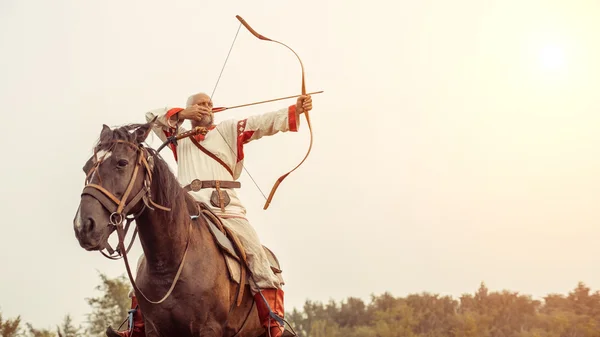 Людина в етнічному одязі їде на коні і прицілюється з лука — стокове фото
