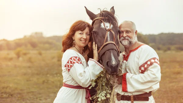 Mature man and woman in ethnic clothes are posing with the horse — Stock Photo, Image