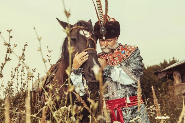 Rei vestido com traje medieval está acariciando seu cavalo no ru — Fotografia de Stock