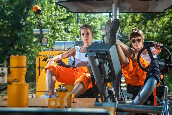 Dos mujeres sexy están operando un tractor enorme en el verano rural — Foto de Stock