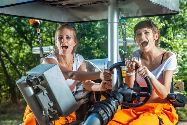 Two funny women are driving a huge tractor together and screamin — Stock Photo, Image