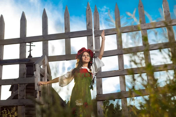 Jovem mulher em russo vestido tradicional está de pé perto de madeira — Fotografia de Stock