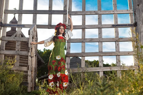 Mladá žena v ruské tradiční šaty stojí poblíž dřevěné — Stock fotografie