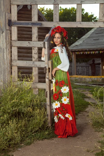 Jovem mulher em russo vestido tradicional está de pé perto de madeira — Fotografia de Stock