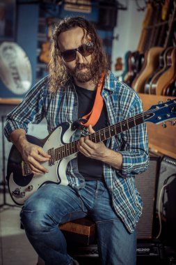 Gitarist bir müzik aleti dükkanında elektro gitarla çalıyor..