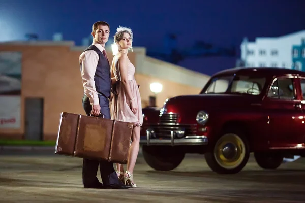 Belo casal com a mala perto do carro vintage . — Fotografia de Stock