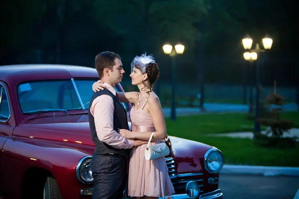 Bonita pareja cerca del coche vintage en el fondo de la ciudad de noche — Foto de Stock