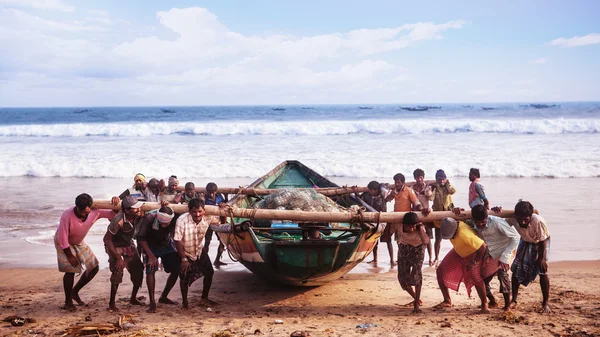 Рыбаки несут лодку на фоне океана . — стоковое фото