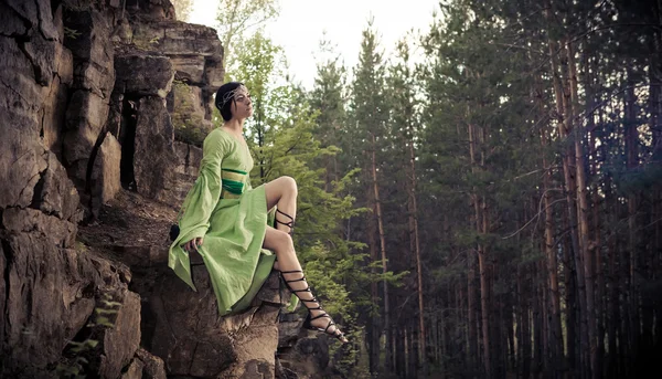 小精灵女人正坐在岩石上。森林的背景. — 图库照片