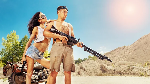 Sexy couple of bikers with guns on the desert background. — Stock Photo, Image