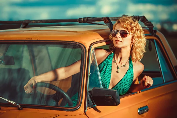 A mulher está a conduzir um carro amarelo velho. Fundo rural . — Fotografia de Stock