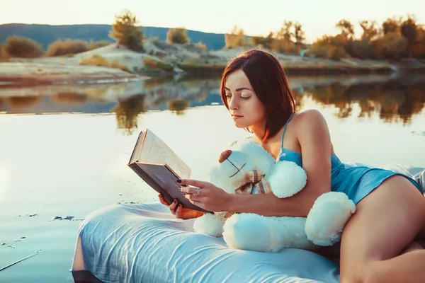 Bella donna è sdraiata sul letto galleggiante e leggere un libro. S — Foto Stock
