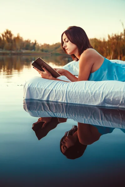 Ładna kobieta jest układanie na pływające łóżko i czytając książkę. S — Zdjęcie stockowe