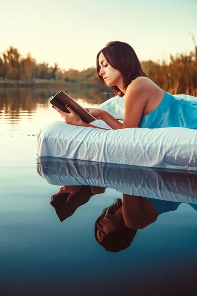 Güzel kadın yatak yüzen ve bir kitap okuma üzerinde yatıyor. S