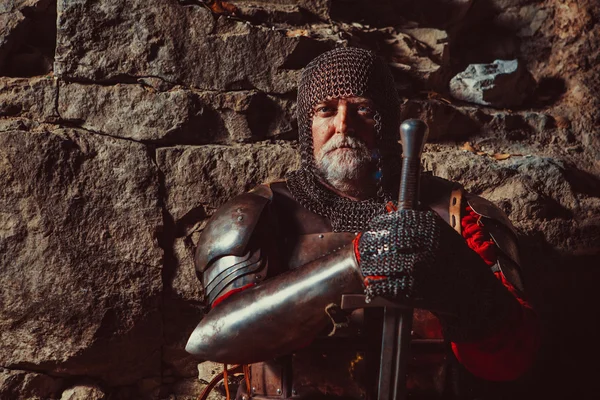 Vieux roi médiéval en armure avec épée sur le fond rocheux — Photo