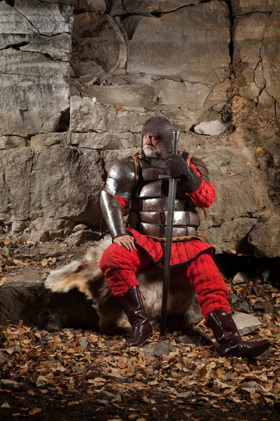 Antiguo Rey medieval en armadura con espada sobre el fondo de las rocas . —  Fotos de Stock