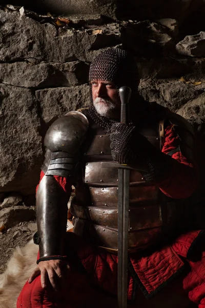 Vieux roi médiéval en armure avec épée est assis sur des fourrures — Photo