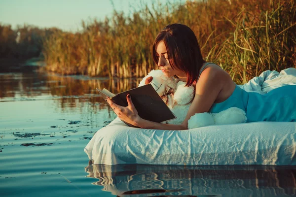 Mulher bonita está deitada na cama flutuante e lendo um livro. S — Fotografia de Stock