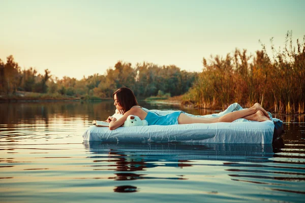 Pretty woman is laying on the floating bed and reading a book. S — Stock Photo, Image