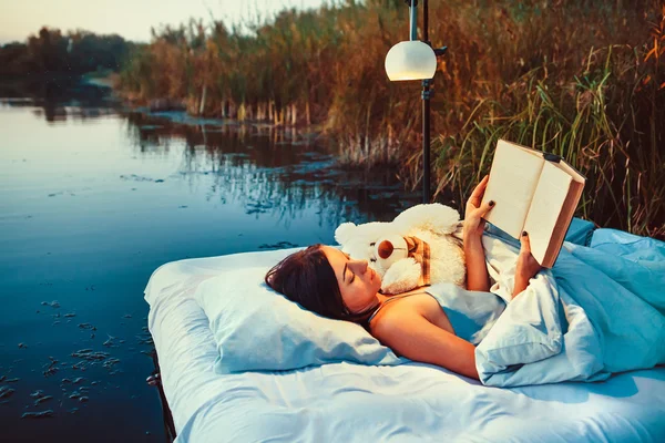 Ładna kobieta jest układanie na dnie pływające z książki i zabawki. — Zdjęcie stockowe