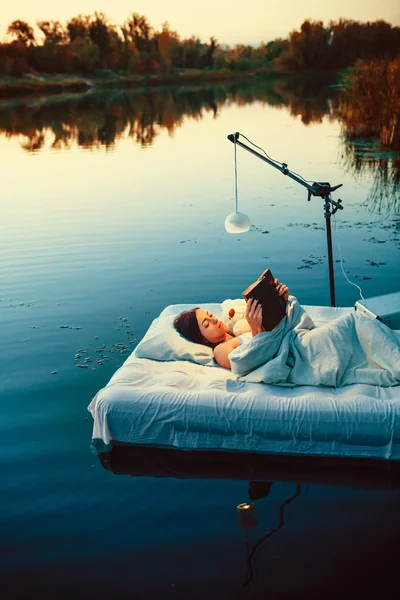 Pretty woman is laying on the floating bed with a book and toy. — Stock Photo, Image