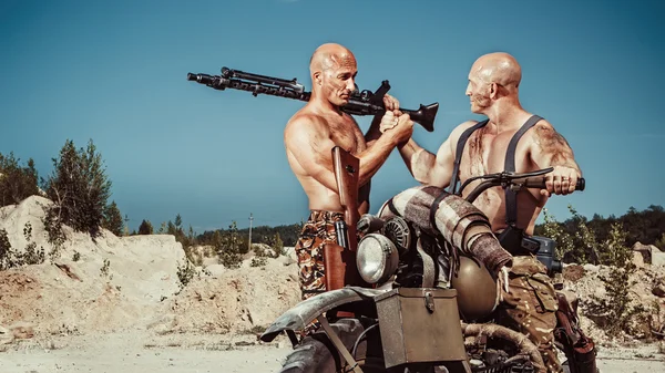 Twee krachtige kale fietsers met geweren op de woestijn achtergrond. — Stockfoto