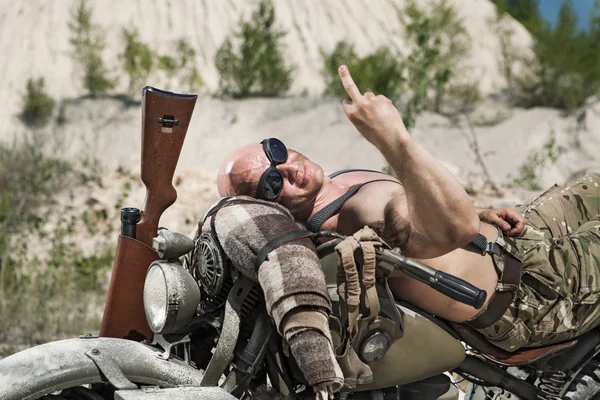 Powerful bald biker is laying on the bike on the desert backgrou — Stock Photo, Image