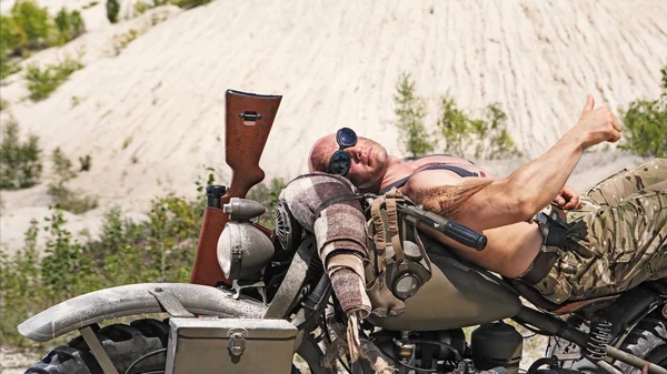 Poderoso motociclista careca está deitado na bicicleta no deserto backgrou — Fotografia de Stock