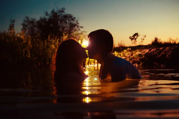 Young couple is kissing in the river on the summer sunset backgr — Stock Photo, Image