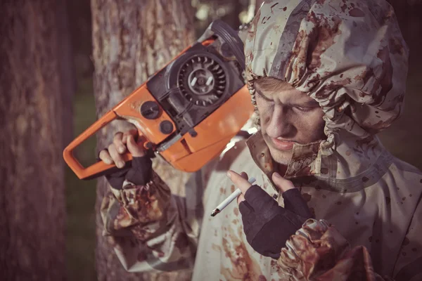 Smoking maniac with the chainsaw dressed in a dirty bloody rainc — Stock Photo, Image