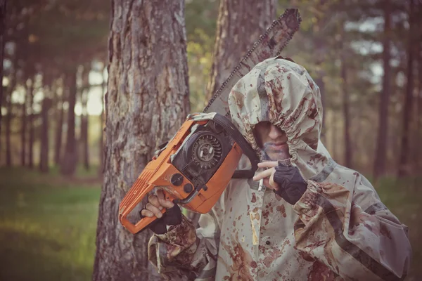 Smoking maniac with the chainsaw dressed in a dirty bloody rainc — Stock Photo, Image