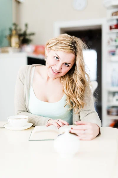 Vacker kvinna läser en intressant bok och dricker kaffe — Stockfoto