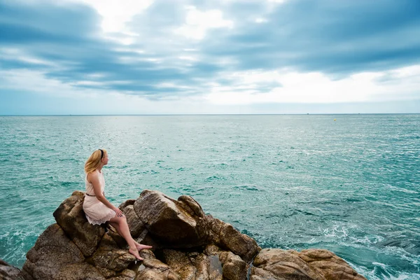 Beautiful young woman sitting on the stone on the seashore — Stock Photo, Image