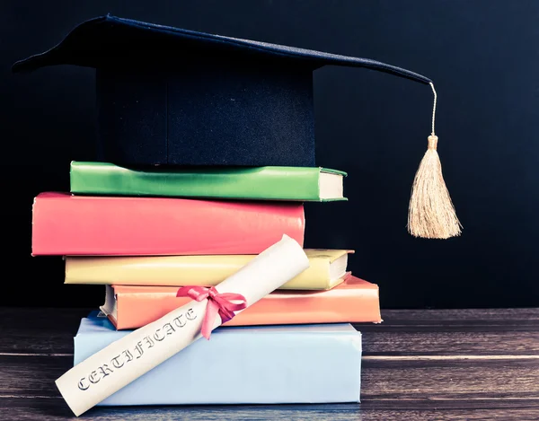 A mortarboard and graduation scroll on books — Stock Photo, Image