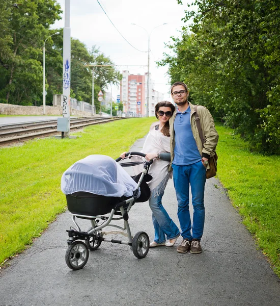Happy man and woman walking with baby pram outdoors — Stock Photo, Image