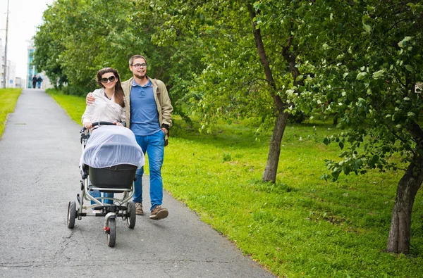 Gelukkig man en vrouw lopen met baby pram buitenshuis — Stockfoto