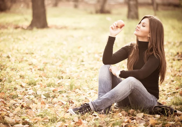 Young woman with apple in autumn park — Stock Photo, Image