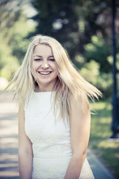 Blonde vrouw in een witte jurk buitenshuis — Stockfoto