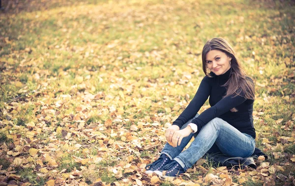 Woman sits on leaves in autumn park — Stock Photo, Image