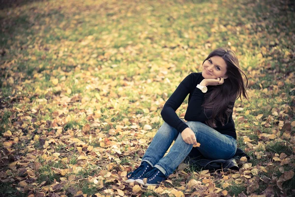 Woman sits on leaves in autumn park — Stock Photo, Image