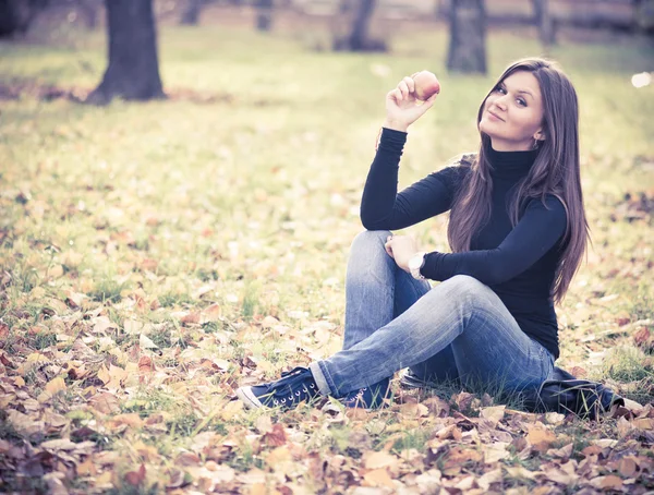 Молодая женщина с яблоком в осеннем парке — стоковое фото