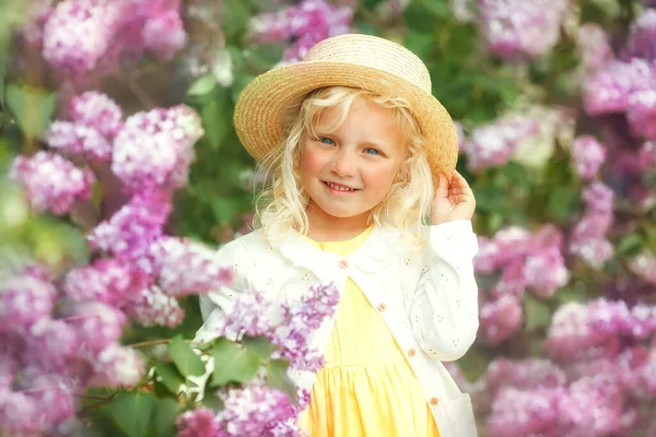 美丽的小女孩 金黄色的卷发在春天的花圃里 图库图片