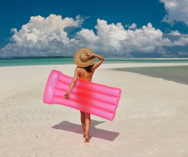 Plajda yürüyen pembe şişme sallı kadın.