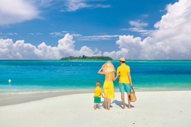 Sahilde bir aile, sarı elbiseli genç bir çift ve üç yaşında bir çocuk. Maldivler 'de yaz tatili.