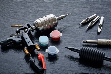 Dövme makinesi, araç gereç ve gereçler siyah tahta üzerine. Dövme stüdyosu.