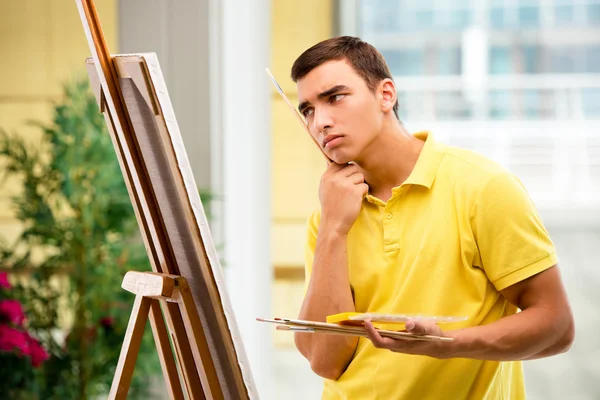 Молодий чоловік художник малює картини в яскравій студії — стокове фото
