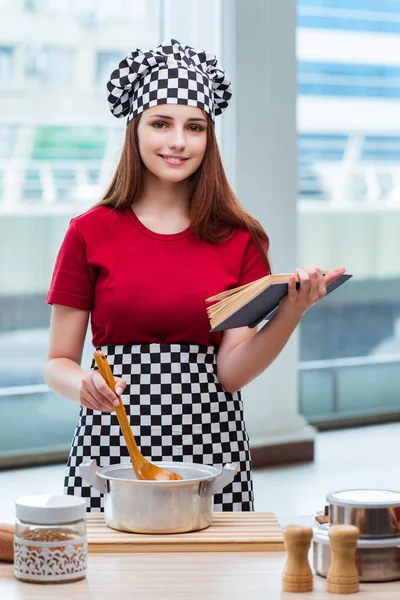 Mladá hospodyňka odkazující na kuchařku — Stock fotografie