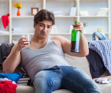 Dağınık bir odada alkol alan sarhoş genç adam.