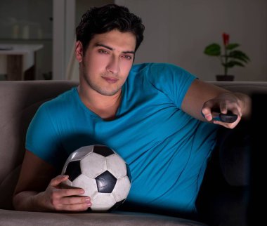 Genç adam gece geç saatlerde futbol seyrediyor.