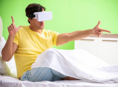Yatak odasında sanal gözlüklü genç adam.
